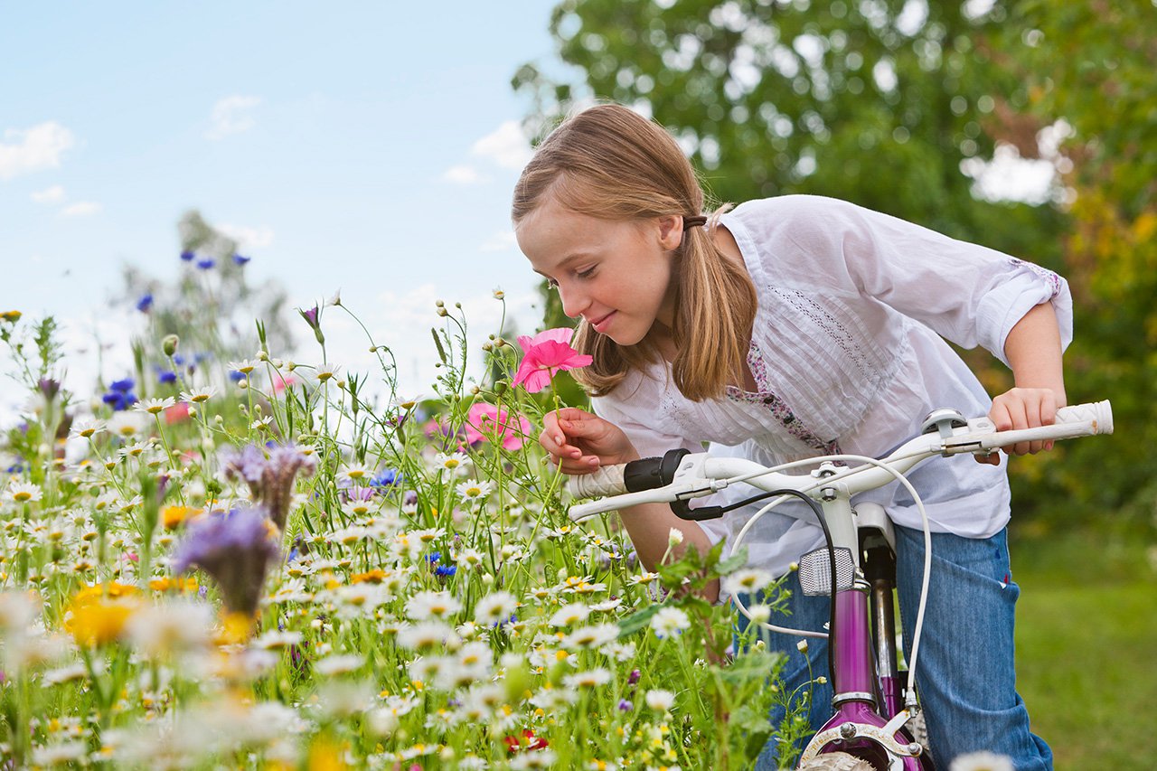Girl-in-countryside-riding-bike-in-field-smelling-wild-summer-flowers